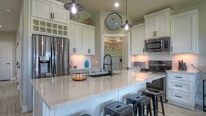 A modern kitchen with white cabinets, stainless steel appliances, a large island with stools, and pendant lighting. - Bayfront Home w/ Pool, Game Room + Walk to Beach & Golf Cart Access Pelicans Perch by Avantstay (Port Aransas)
