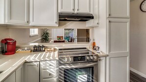 Una cocina con gabinetes blancos, una estufa de acero inoxidable y una cafetera.