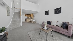 A spacious living area with a staircase, a kitchen in the background, and a sofa with cushions. - Loft-style CBD 1-bed With Rooftop Terrace & BBQ (Canberra)