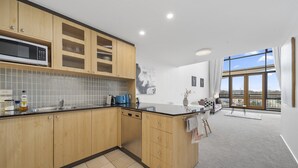 A modern kitchen with wooden cabinets, a microwave, and a large window offering a view of the city. - Loft-style CBD 1-bed With Rooftop Terrace & BBQ (Canberra)