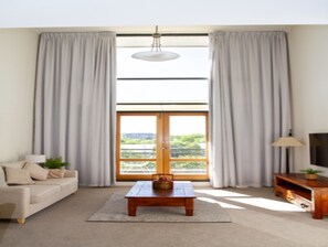 A living room with a sofa, a coffee table, a TV stand, and a large window with curtains.