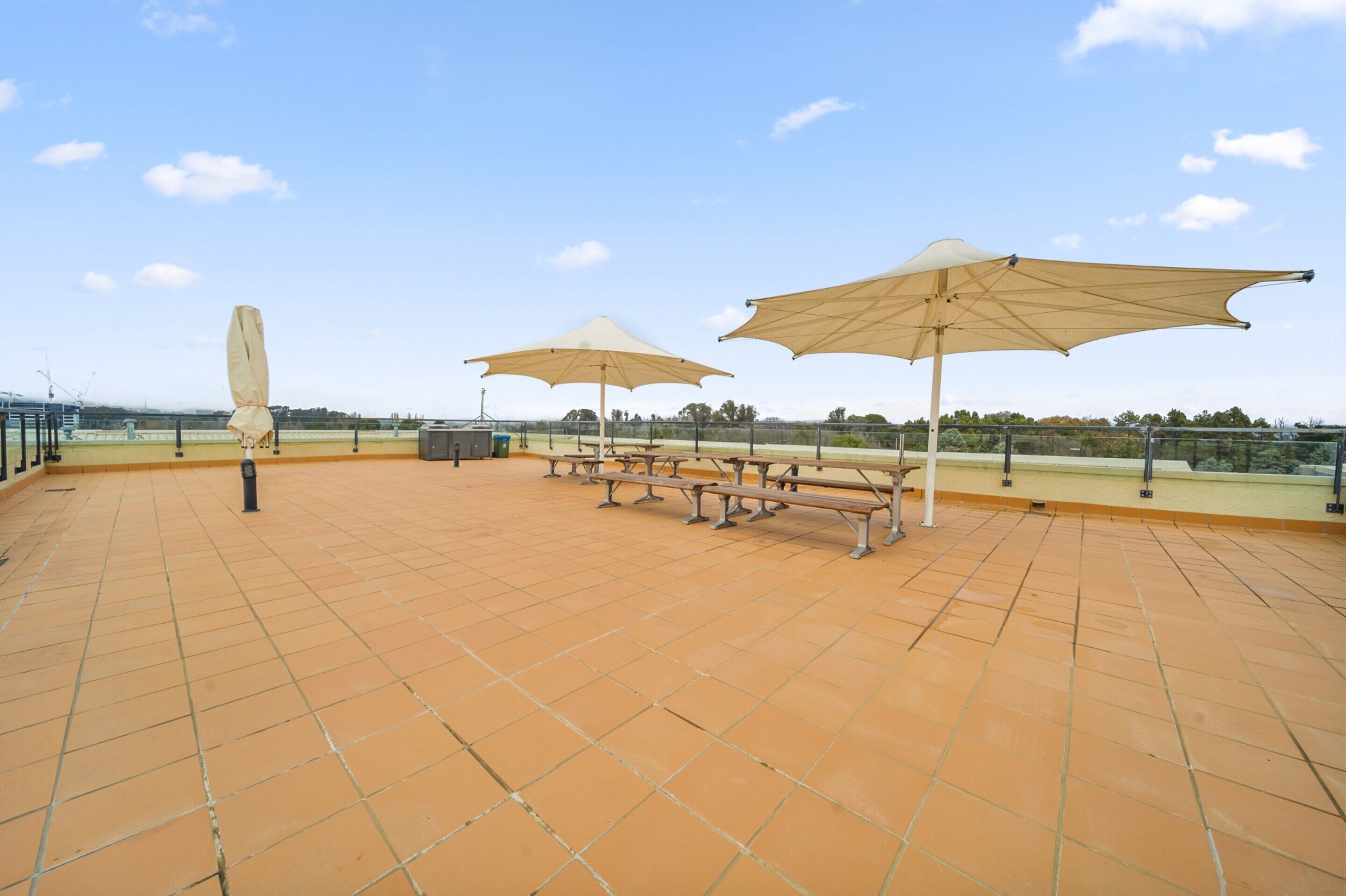 Une terrasse extérieure dotée d’un sol carrelé, de tables de pique-nique et de grands parasols.
