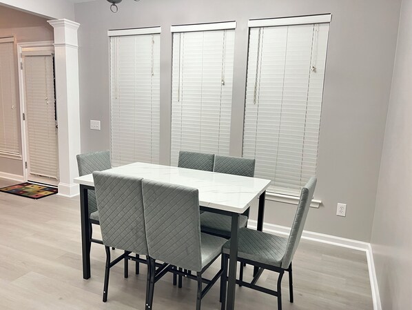 A dining area with a white table and four chairs, a door with a white frame, and a window with blinds. - Expansive 5BR Home steps away from Trader Joe's (Charlotte)