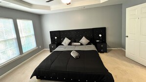 Une chambre avec un grand lit, un ventilateur de plafond et une table de chevet.