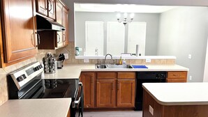 Une cuisine moderne avec des meubles en bois, un four encastré, un lave-vaisselle et une grande fenêtre équipée de stores.