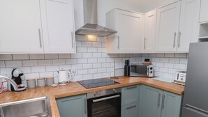 A modern kitchen with white cabinets, a built-in oven, a microwave, and a toaster. - Nobles Nook (Seahouses)