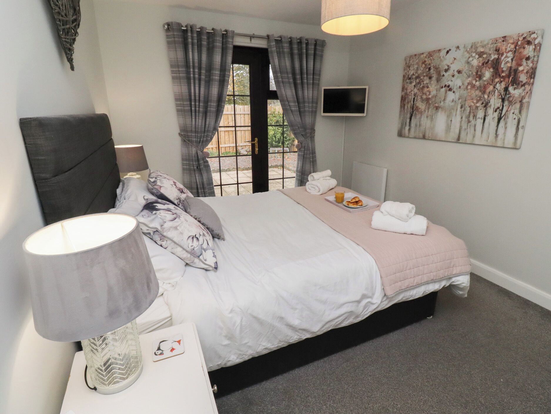 A bedroom with a bed, a bedside table with a lamp, a TV, and a painting on the wall.
