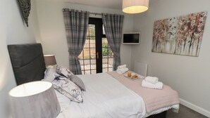 A bedroom with a bed, a bedside table with a lamp, a TV, and a painting on the wall. - Nobles Nook (Seahouses)
