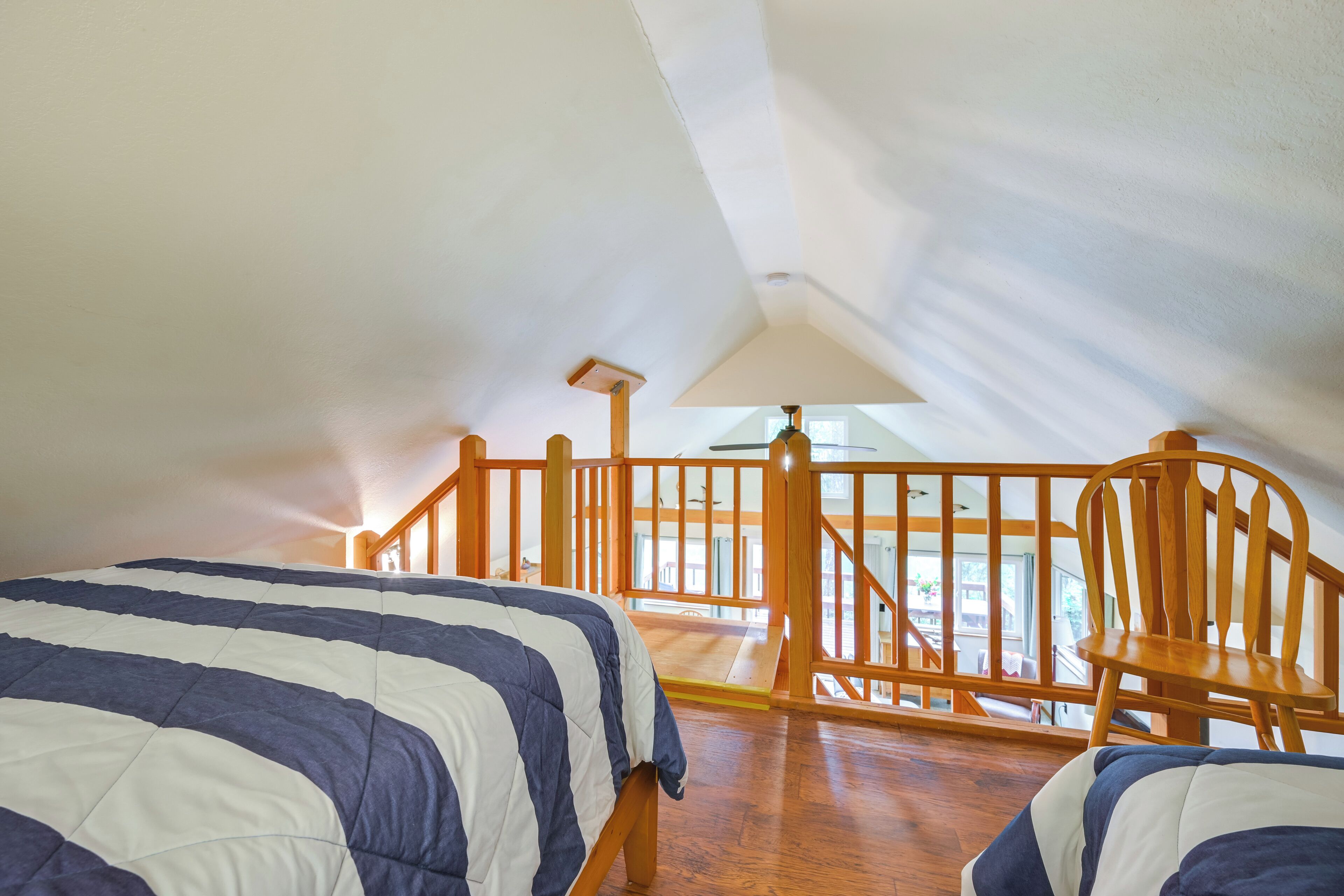 Ein Schlafzimmer mit hölzernem Bettgestell, einem Holzstuhl und Blick ins Freie durch ein Fenster.