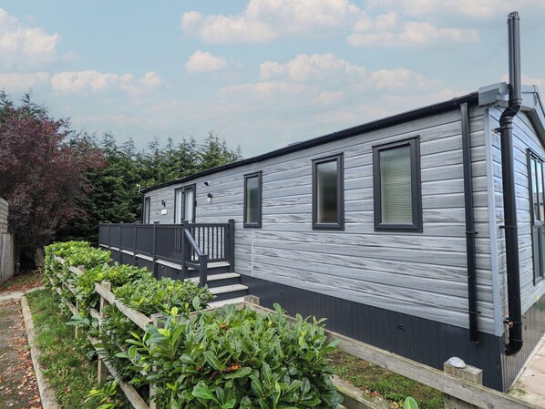 A mobile home with a wooden deck, a small porch, and a garden area with green plants.