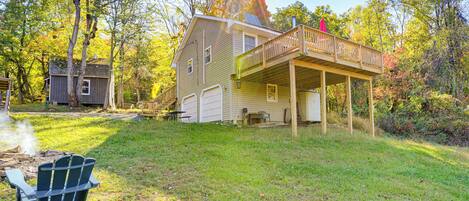 A house with a deck, a garage, and a small shed in a wooded area.