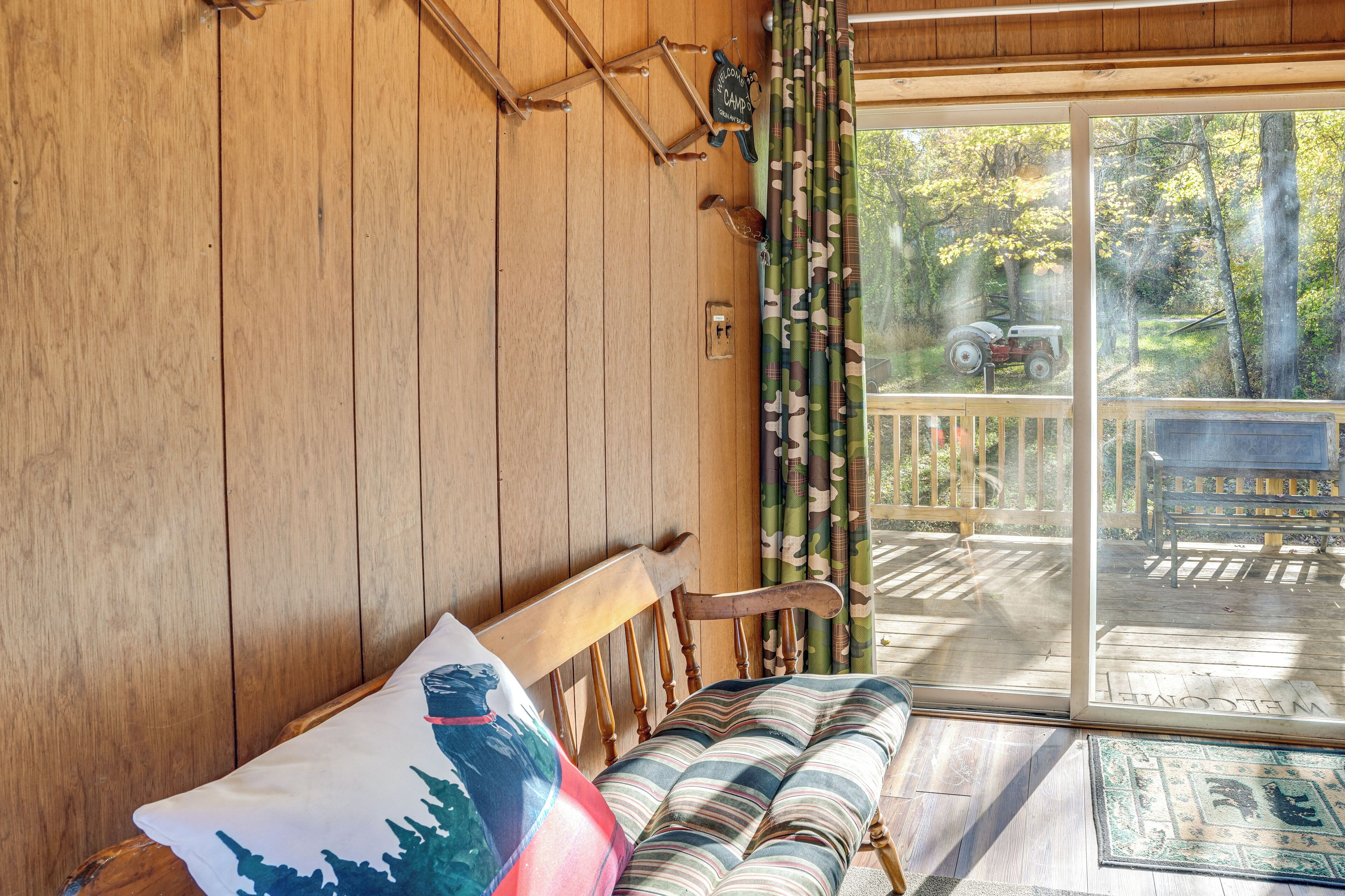 A wooden interior with a bench, a door leading to an outdoor deck, and a view of a vehicle outside.