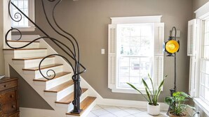 Una escalera con barandilla de metal negro, paredes blancas y una ventana con contraventanas.