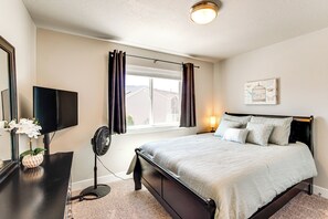 Un dormitorio con cama, televisor, ventilador, ventana con cortinas y una lámpara fijada a la pared.