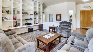 A living room with a sectional sofa, a coffee table, a bookshelf, and a grey armchair. - Groups Welcome! Home w/ Pool + Patio in N Phoenix (Phoenix)