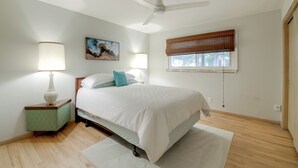 Quarto com cama, luminárias de cabeceira, ventilador de teto, janela com persianas e um quadro na parede.