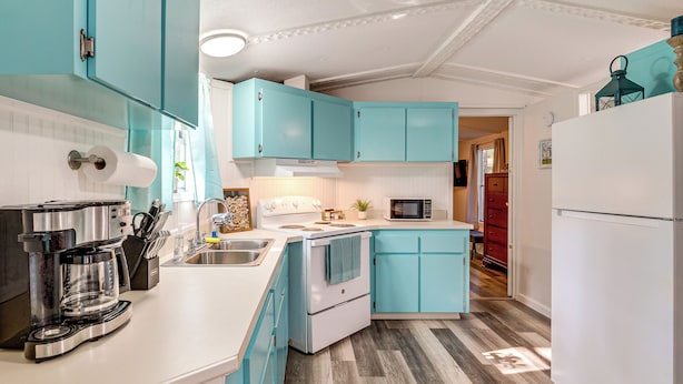 Une cuisine avec des armoires de couleur turquoise, un four blanc, une machine à café et un four à micro-ondes.