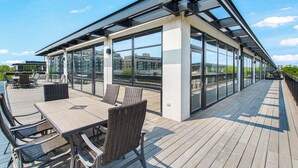A modern outdoor deck with glass walls, wicker furniture, and a view of the city skyline. - Extended Stay: Walk to UIC Campus & Train! (Chicago)