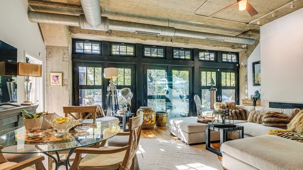 A spacious living area with a glass dining table, wooden chairs, a sofa, and a coffee table. Large windows allow natural light to fill the room. - Extended Stay: Walk to UIC Campus & Train! (Chicago)