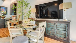 A dining area with a glass table, wooden chairs, a plant, and a vintage cabinet. - Extended Stay: Walk to UIC Campus & Train! (Chicago)