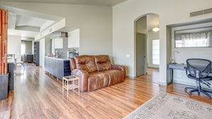 A spacious living area with a leather sofa, wooden flooring, a small side table, and a desk with a chair. - Families Welcome! Dog-Friendly Glendale Home (Sun City West)
