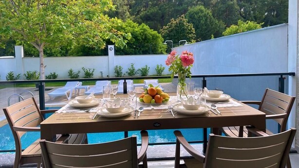 A dining table set for six with a view of a swimming pool and greenery.