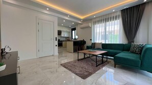 A modern living room with a green sofa, a coffee table, and a kitchen in the background.