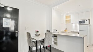 A modern kitchen with white cabinetry, a microwave, and a refrigerator. There is a dining area with a table and chairs. - 1-bed Apartment in Central Melbourne (Melbourne)