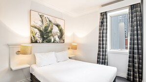 A hotel room with a bed, two bedside lamps, a wall-mounted artwork, a window with curtains, and a nightstand. - 1-bed Apartment in Central Melbourne (Melbourne)