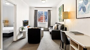 A modern hotel room with a bed, a desk, a sofa, a small table, and a TV. - 1-bed Apartment in Central Melbourne (Melbourne)