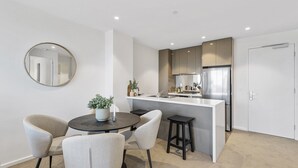 A modern kitchen with a central island, a dining area with four chairs, and a round mirror on the wall. - Elegant 2-bed Apartment With Balcony & City Views (Melbourne)
