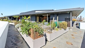 A modern building with a flat roof, large windows, and a paved walkway with planters. - Elegant Inner-city 1-bed With Rooftop Dining (Brisbane)