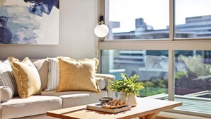 A modern living room with a sofa, a coffee table with decorative items, and a large window offering a city view. - Elegant Inner-city 1-bed With Rooftop Dining (Brisbane)