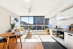 A modern kitchen with a large window, a dining area with a table and chairs, and a sofa. - Elegant Inner-city 1-bed With Rooftop Dining (Brisbane)
