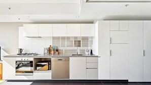 A modern kitchen with white cabinets, a built-in oven, microwave, and dishwasher. - Elegant Inner-city 1-bed With Rooftop Dining (Brisbane)