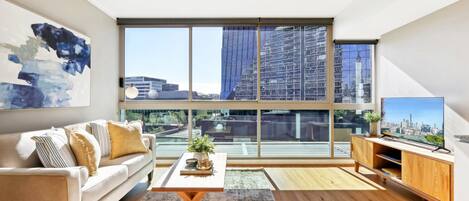 A modern living room with a large window, a sofa, a coffee table, and a TV on a wooden stand.