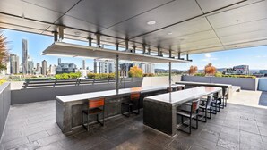 An outdoor bar area with a city view, featuring a long counter and multiple chairs. - Elegant Inner-city 1-bed With Rooftop Dining (Brisbane)