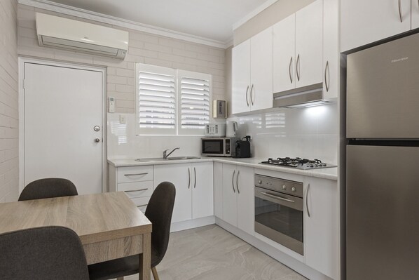 A modern kitchen with white cabinets, stainless steel appliances, and a wooden dining table. - Bright 2-bed Apartment Steps From Largs Bay Beach (Adelaide)
