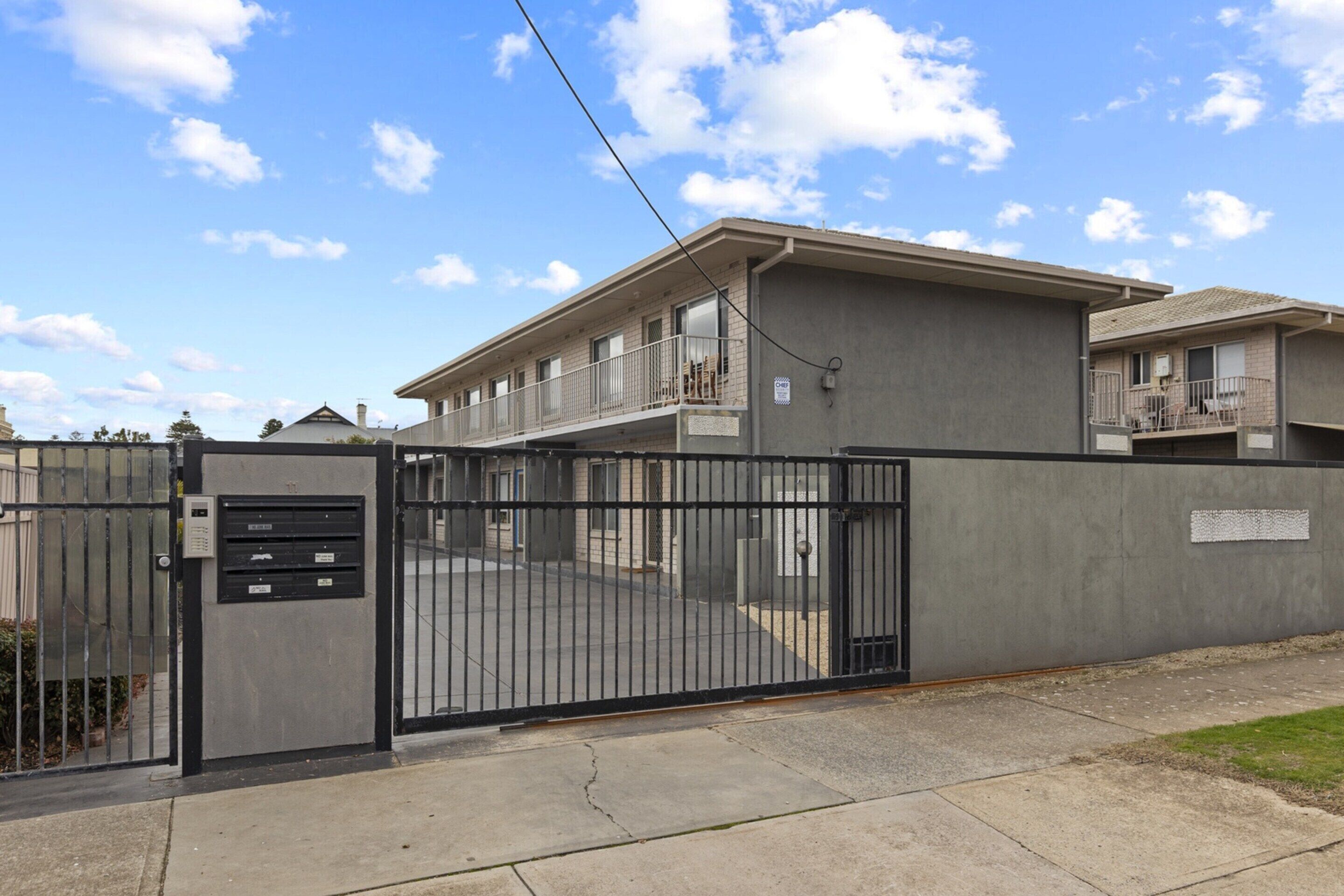A gated building with a flat roof, a balcony on the second floor, and a security gate.