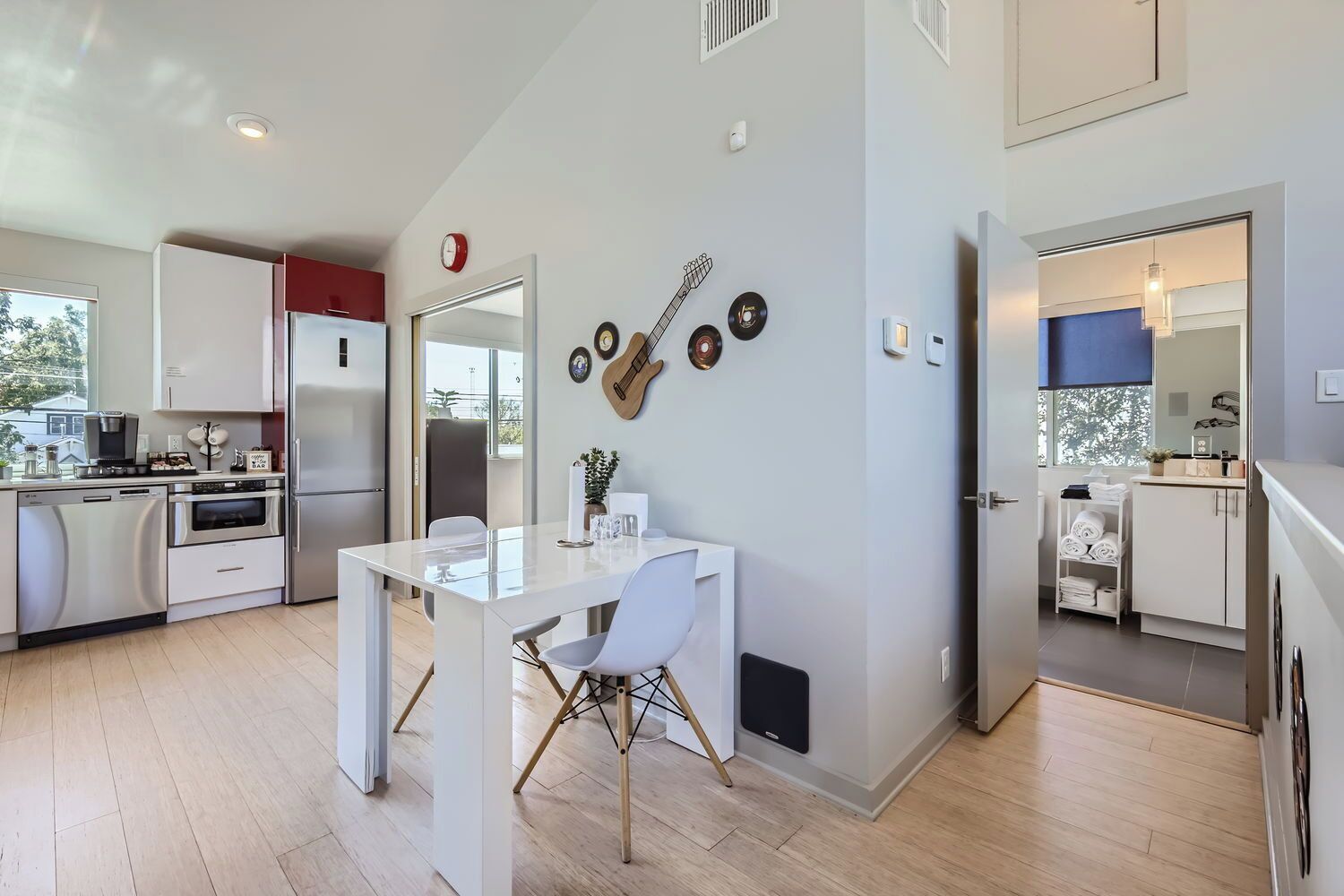 A modern kitchen with white cabinetry, a dining area with a white table and chairs, and a living area with a blue accent wall and a mirror.