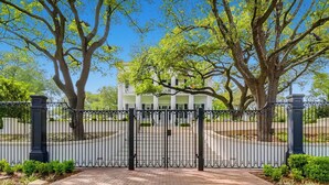 A gated entrance with a white building, large trees, and a clear blue sky. - 4BR Home, Hot Tub, Hypedome, 3-minutes to Downtown Austin! (Austin)