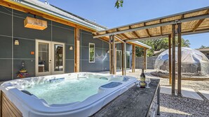 A hot tub in a covered outdoor area with a pergola, a wooden deck, and a greenhouse in the background. - 4BR Home, Hot Tub, Hypedome, 3-minutes to Downtown Austin! (Austin)