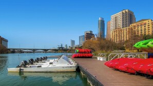 A riverfront with a dock, a boat, and a row of red kayaks. - 4BR Home, Hot Tub, Hypedome, 3-minutes to Downtown Austin! (Austin)