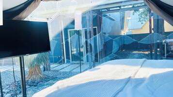 Quarto moderno com divisória de vidro, cama e vista para o exterior.