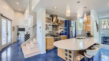 Cozinha moderna com ilha central, eletrodomésticos de aço inoxidável e iluminação pendente.
