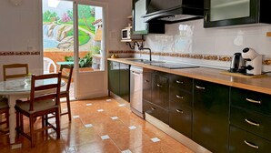 A kitchen with a dining area, featuring a window with a view of a garden, a microwave, a coffee maker, and a dishwasher. - Casa Luz de Azahar - Ole Solutions (Jerez de la Frontera)
