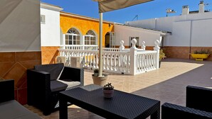 A covered outdoor patio with a table and chairs, a white fence, and a yellow wall in the background. - Casa Luz de Azahar - Ole Solutions (Jerez de la Frontera)