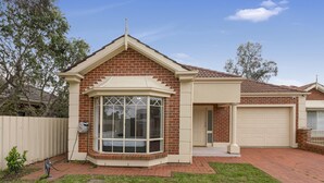 Une maison d’habitation avec une façade en briques, une baie vitrée, un garage et une cour clôturée.