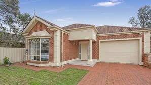 Une maison de plain-pied avec une façade en briques, un garage et un petit porche à l’avant.