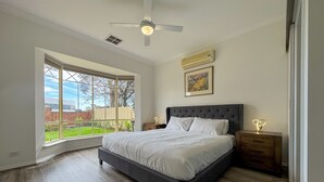 Une chambre avec un grand lit, un ventilateur de plafond, une fenêtre donnant sur l’extérieur et une table de chevet avec une lampe.
